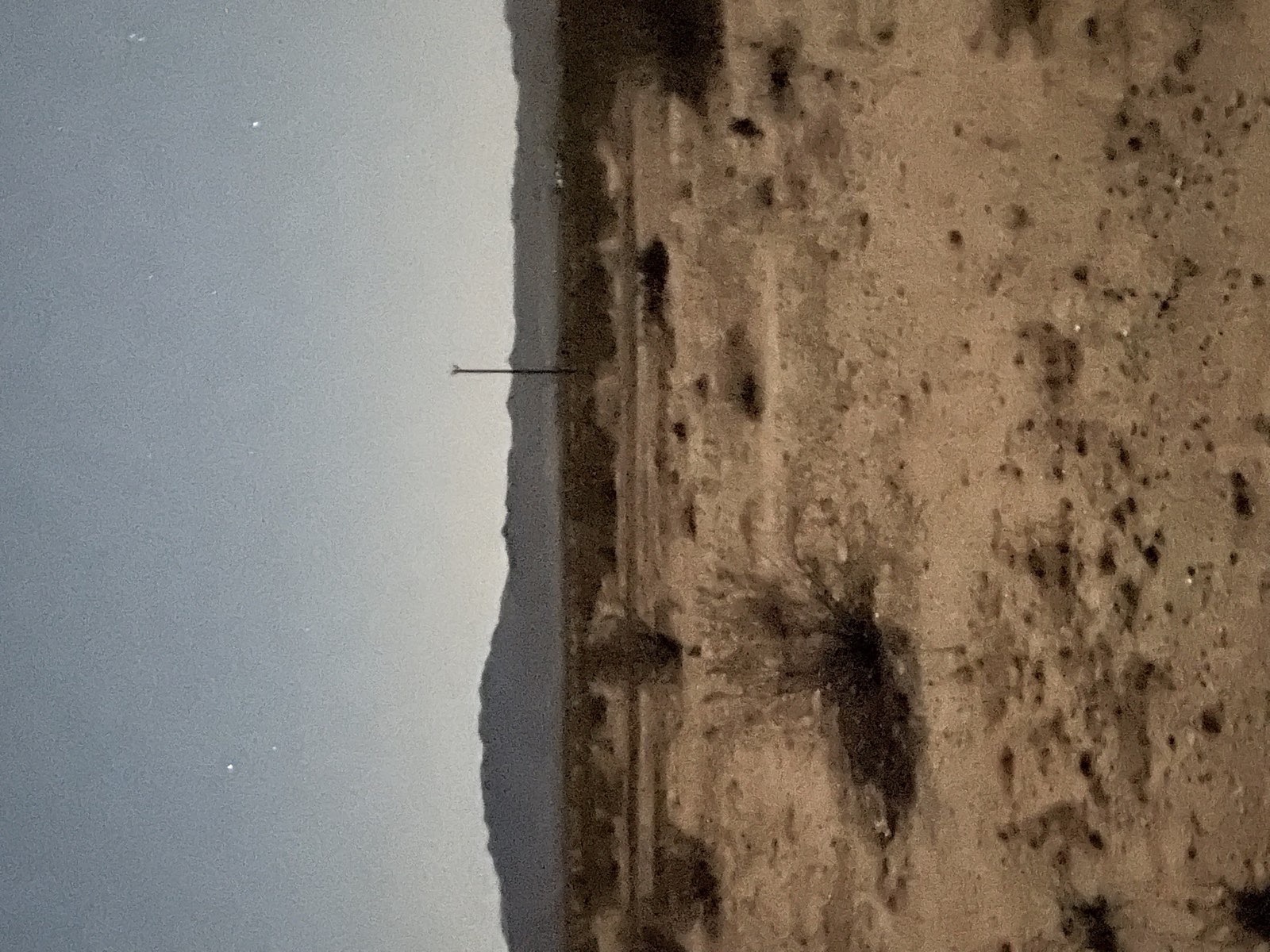 The dark ridge line at night under a grey-blue sky, a single thin antenna standing against the last light